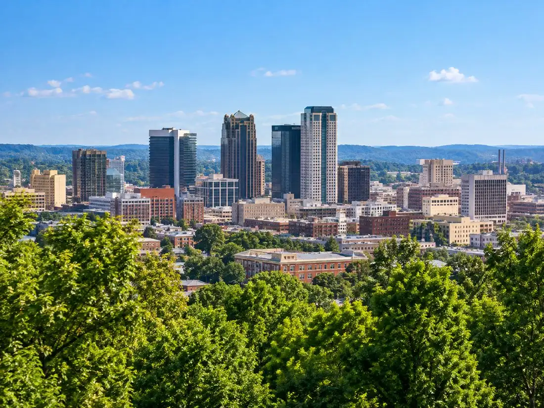 The Birmingham, Alabama skyline rising above green treetops under a clear blue sky